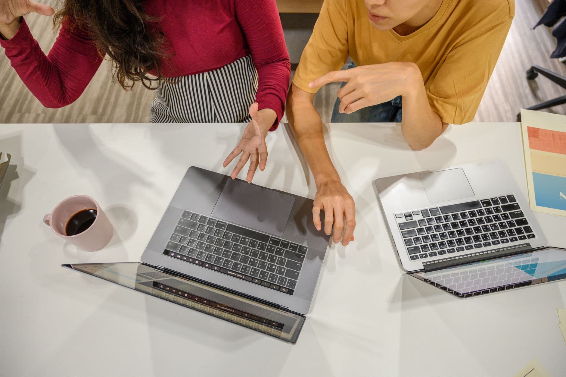 Two professionals engage in a collaborative discussion with laptops and coffee at a modern workspace.