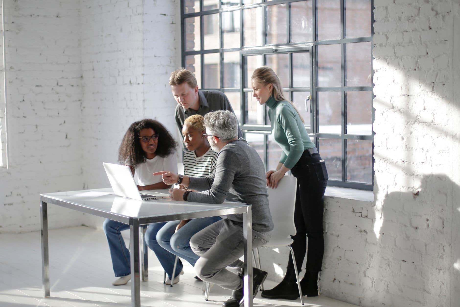 Diverse expressive coworkers sitting at table and looking at screen of laptop while working on project together