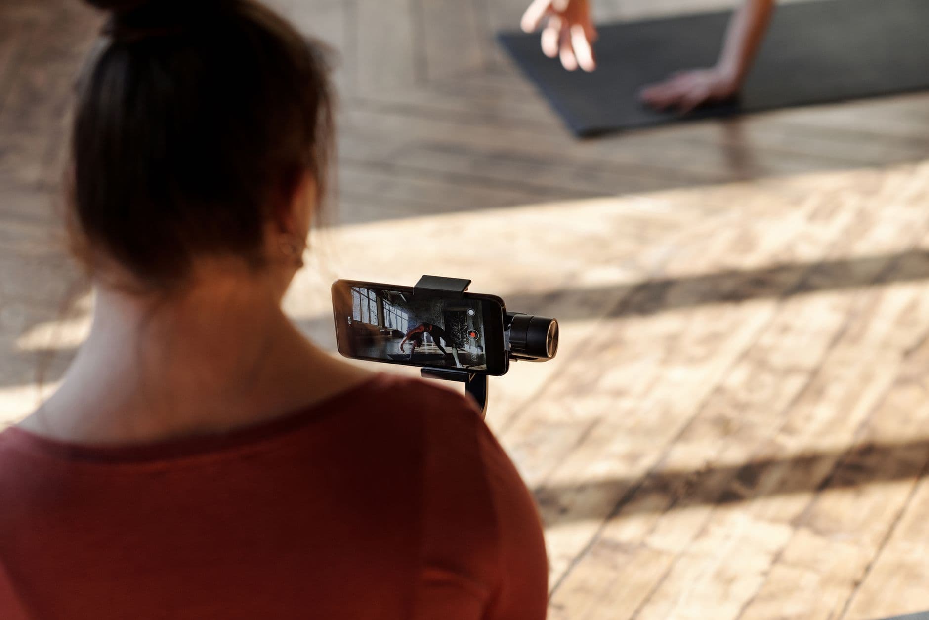 Woman recording a yoga session indoors using a smartphone on a stand, with focus on technology and fitness.