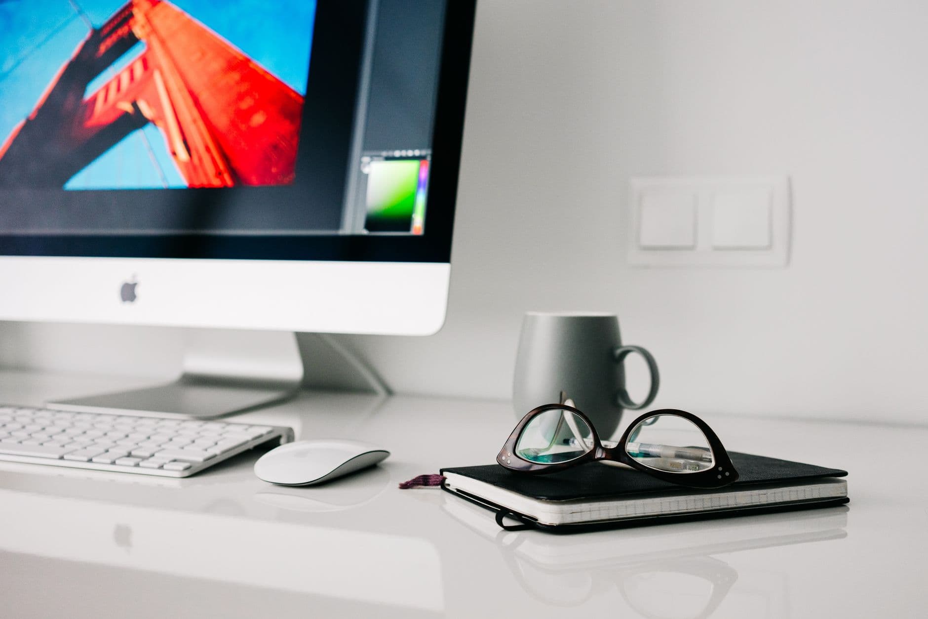 Stylish office workspace featuring a desktop computer, glasses, and notebook.