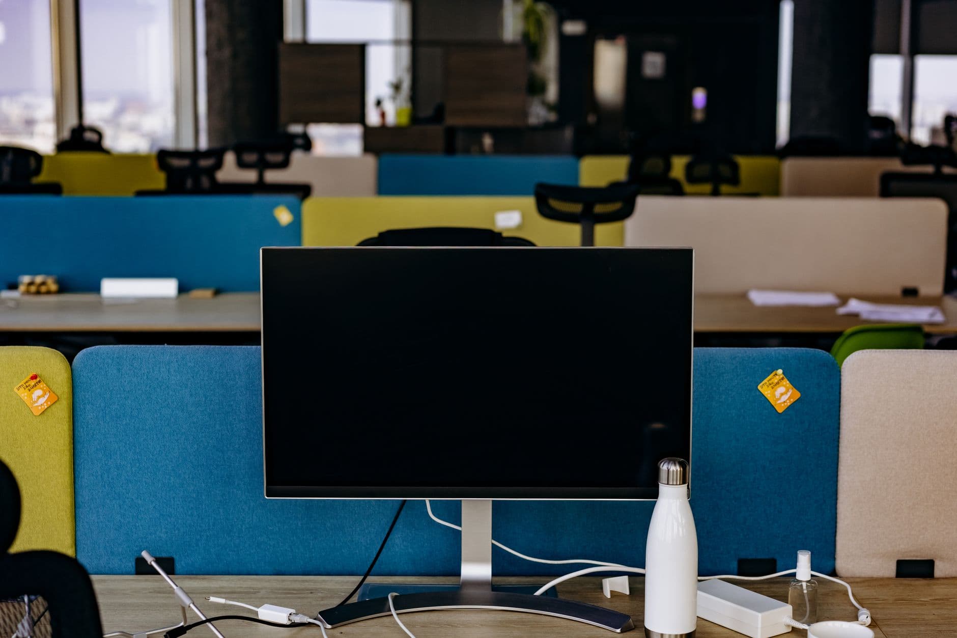 A contemporary office setup featuring a monitor, partitions, and accessories on a desk within an open-plan office.