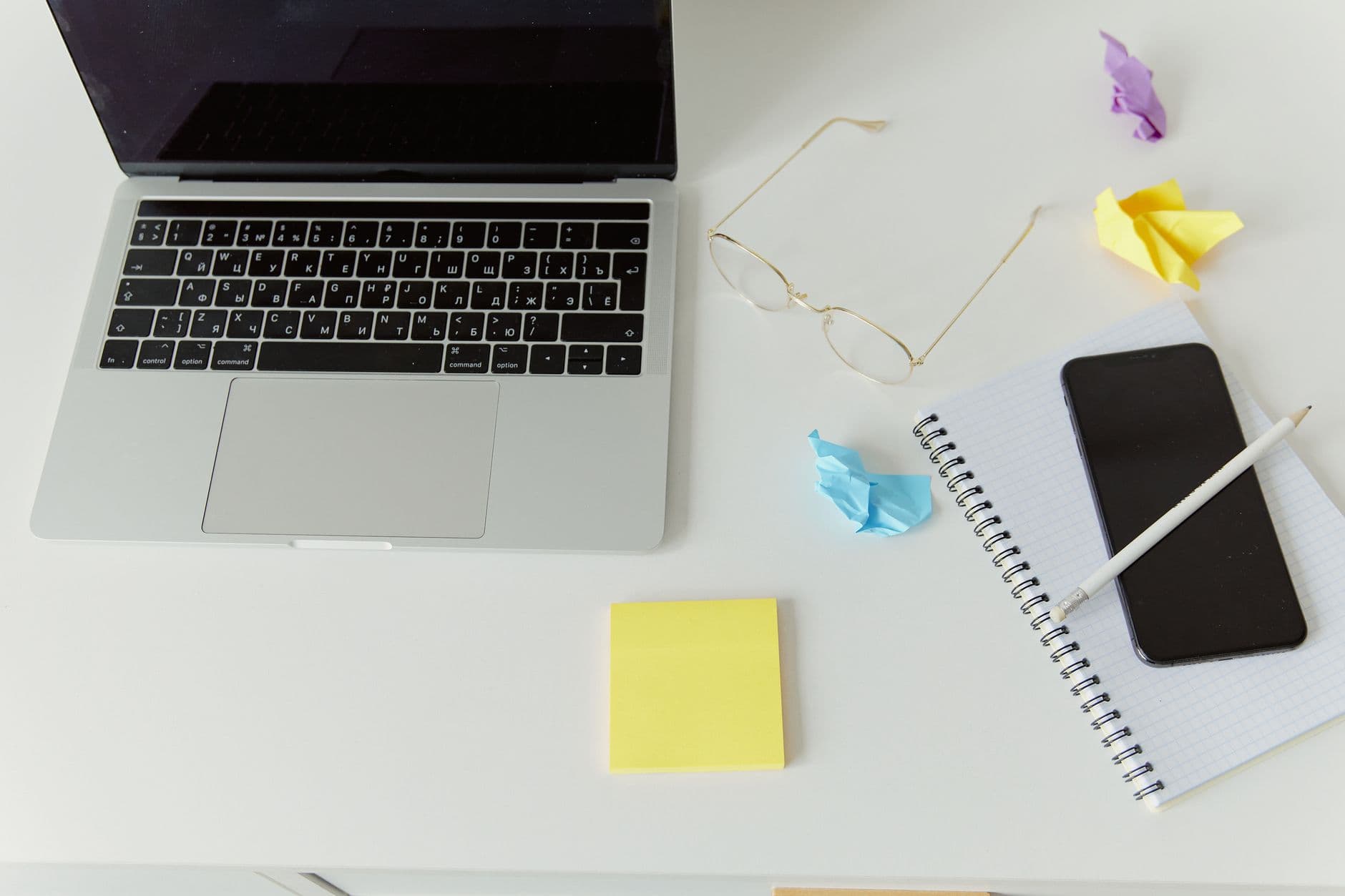 A minimalistic office desk with a laptop, notepad, and crumpled paper for productivity.