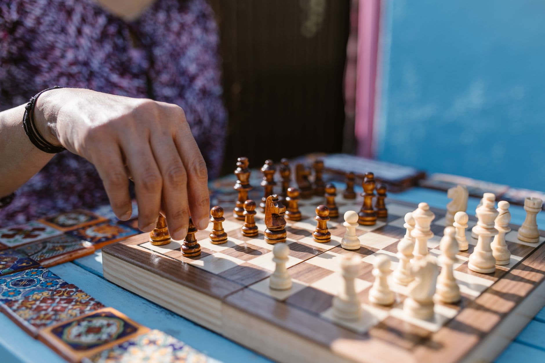 A hand moving wooden chess pieces on a chessboard outdoors in daylight.