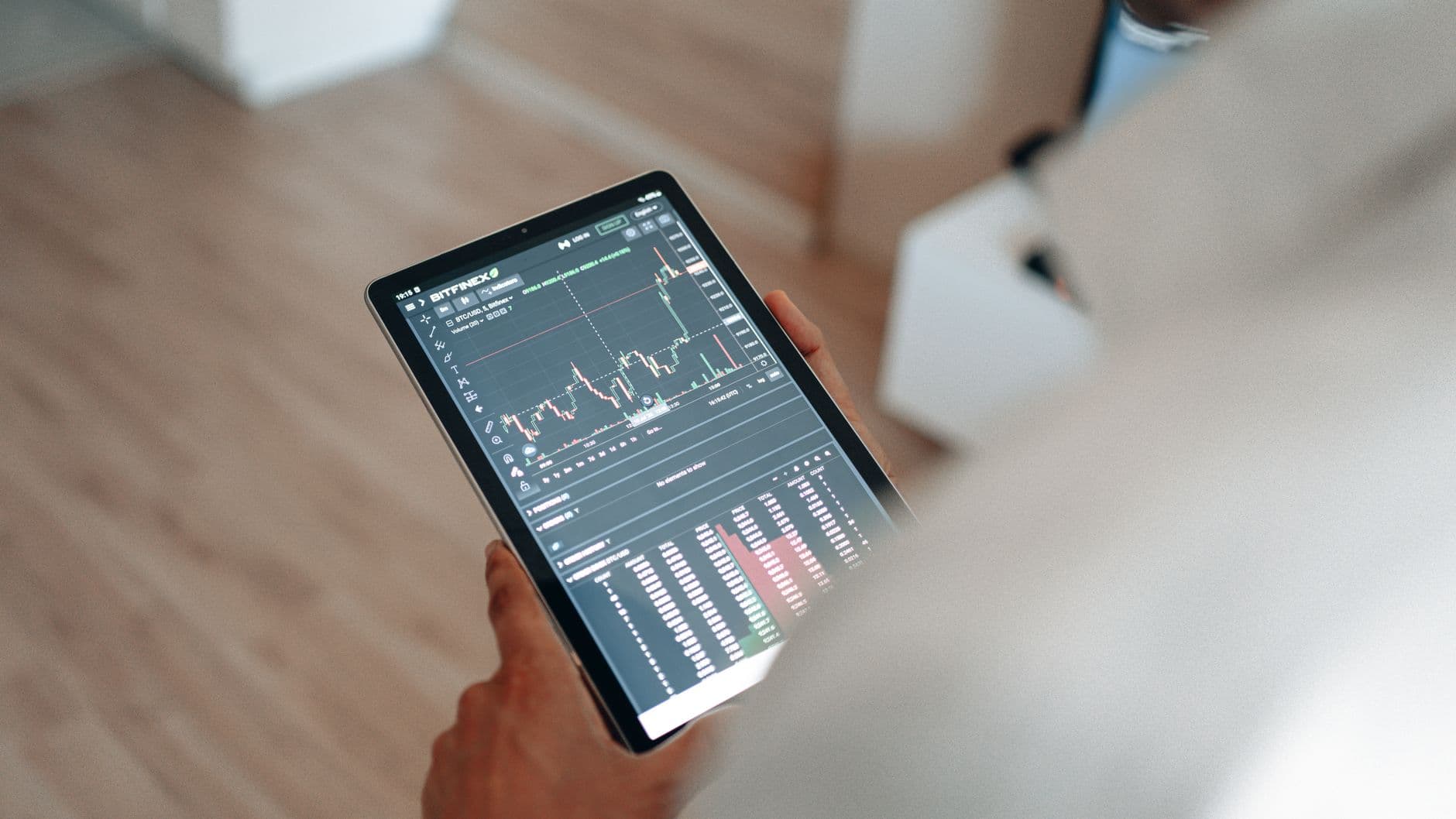 Close-up of person using a tablet displaying trading graphs indoors.