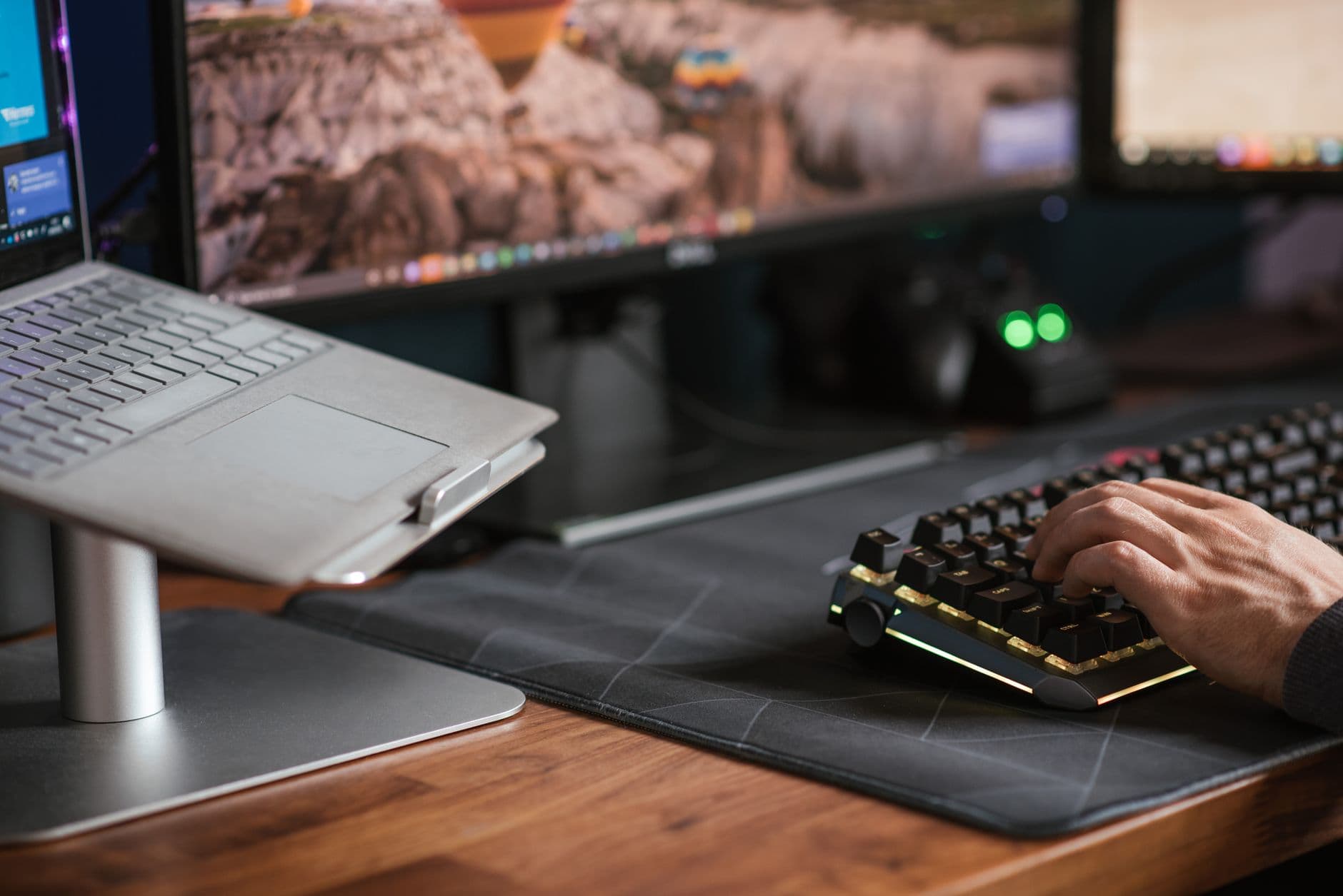 Crop anonymous male working on computer and typing on backlit keyboard placed near contemporary laptop on stand