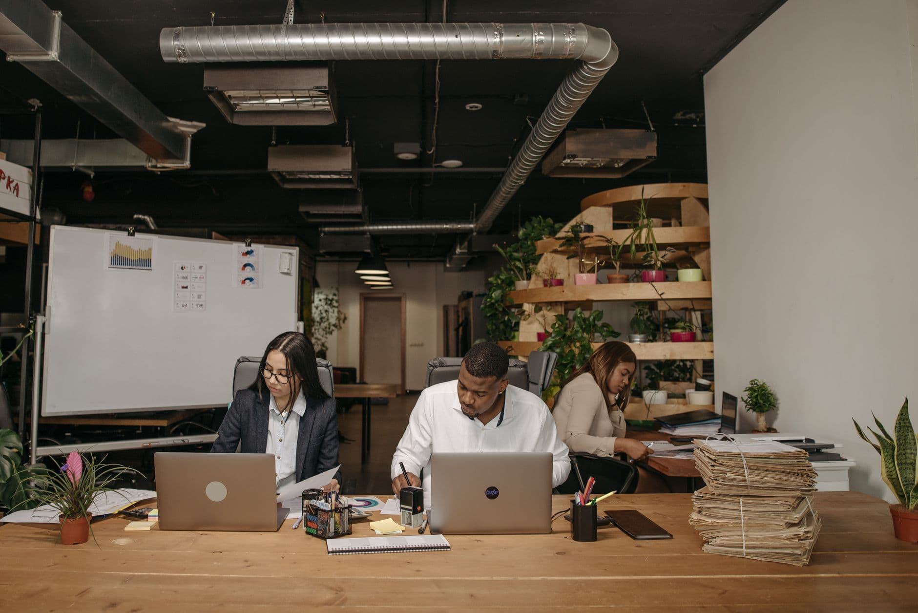 Three professionals focused on work in a stylish office with laptops and documents.