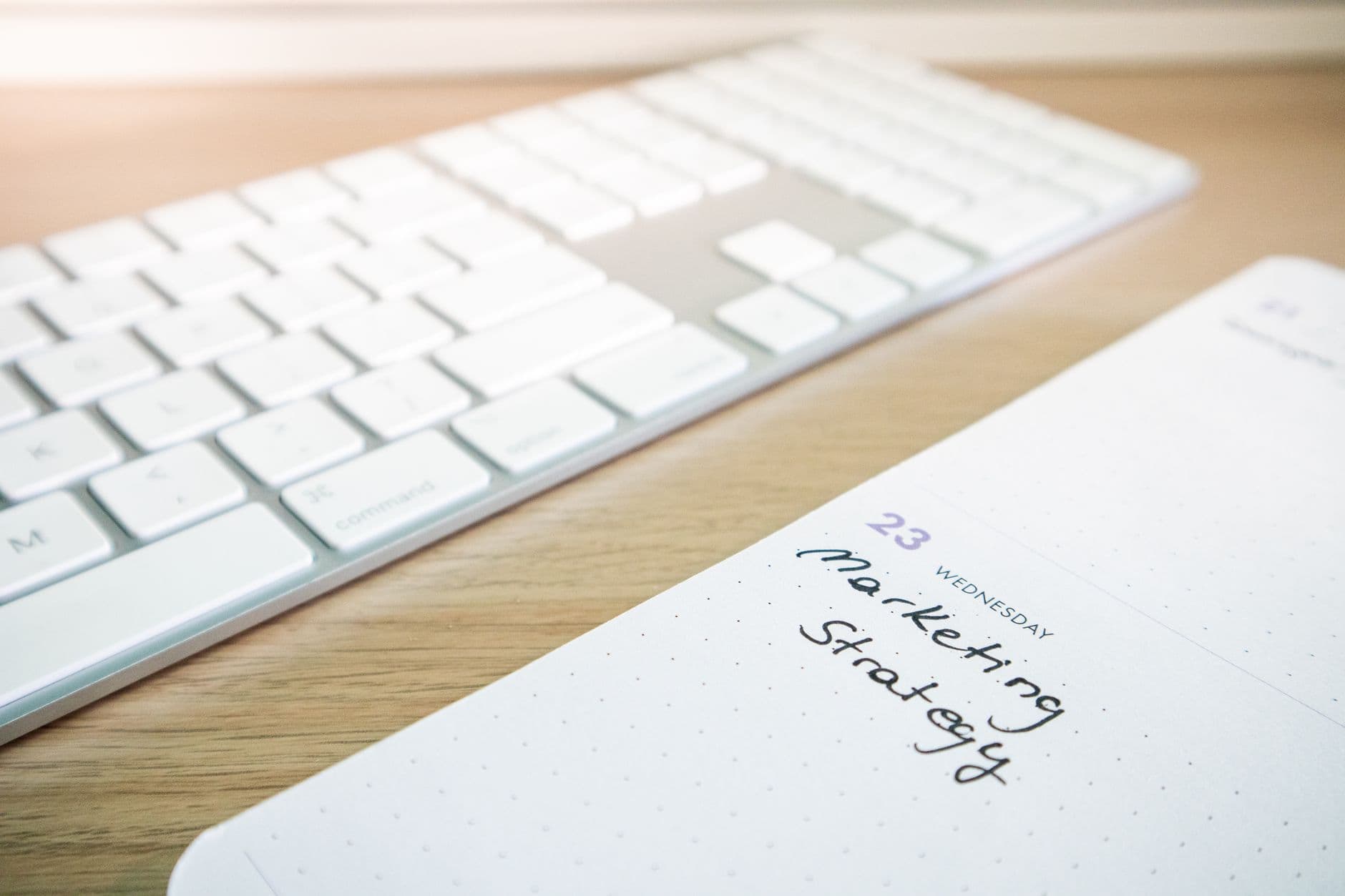 Notebook with marketing strategy note alongside a keyboard on a wooden desk.
