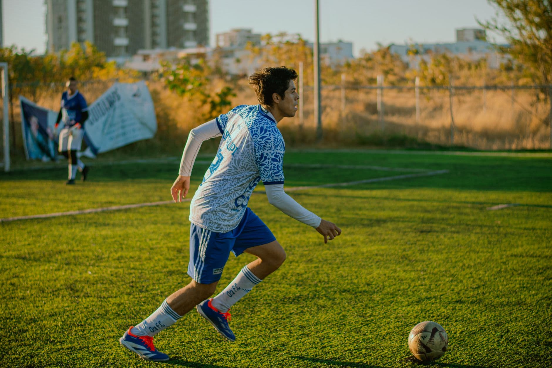 Teen soccer player dribbles the ball on a sunny day outdoor field.