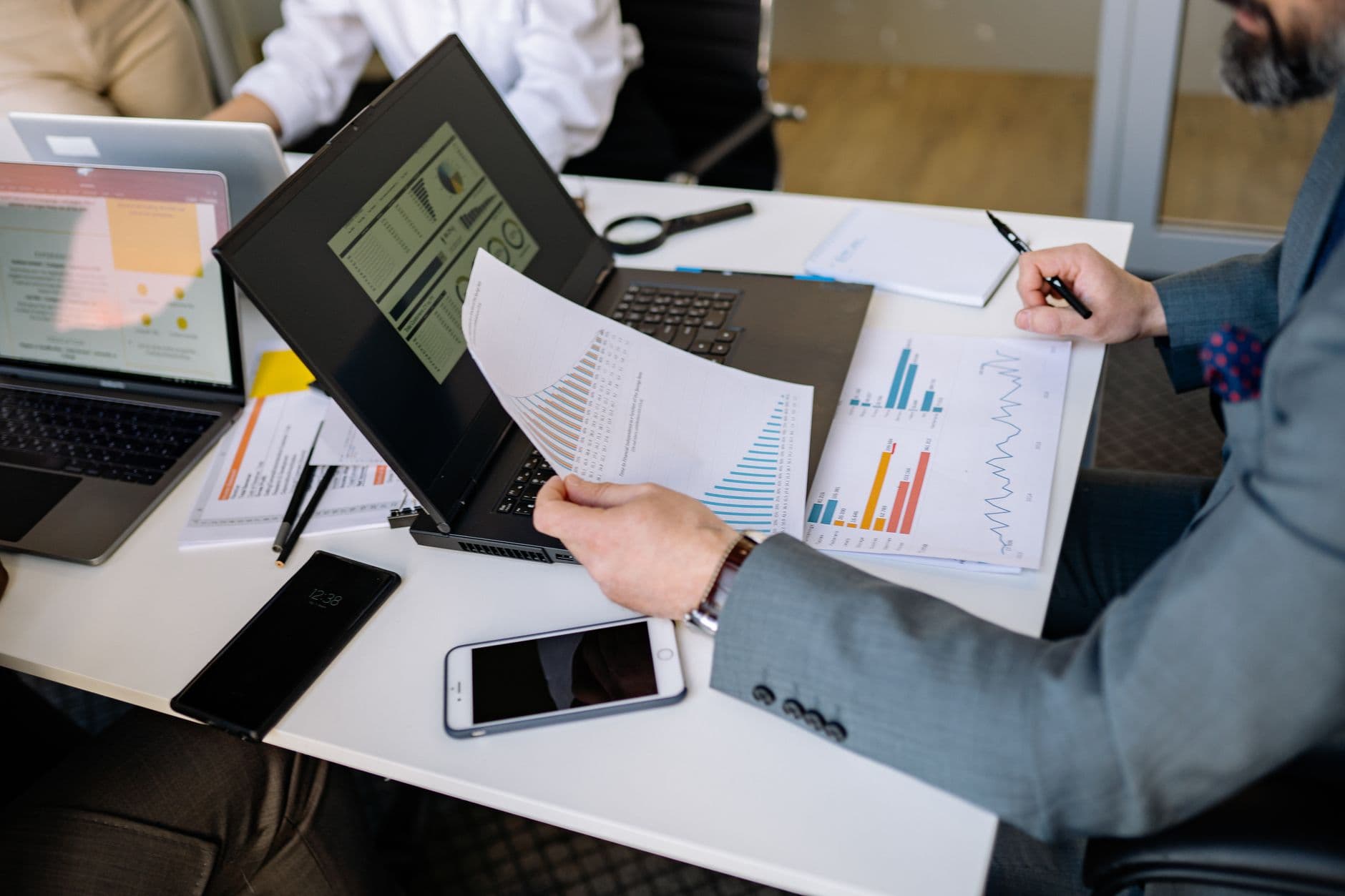 Professionals analyzing charts and graphs on laptops during a business meeting.